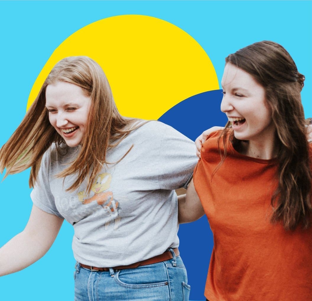 Two friends laughing together, arm in arm, in front of a yellow sun